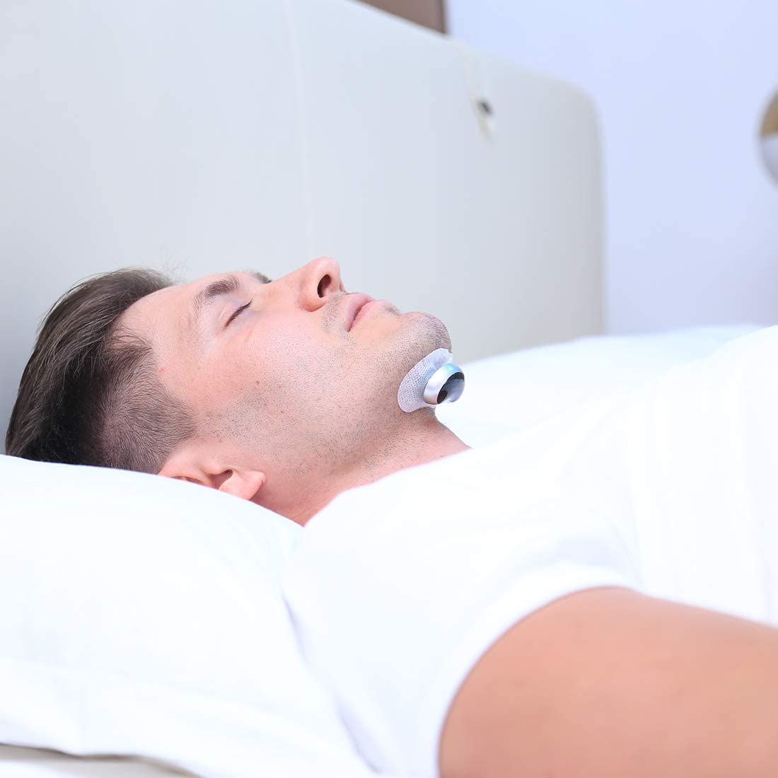 Man lying down with a device on his neck, possibly for medical or wellness purposes.