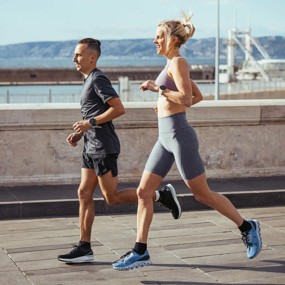 Two people running outdoors on a sunny day with a scenic background.