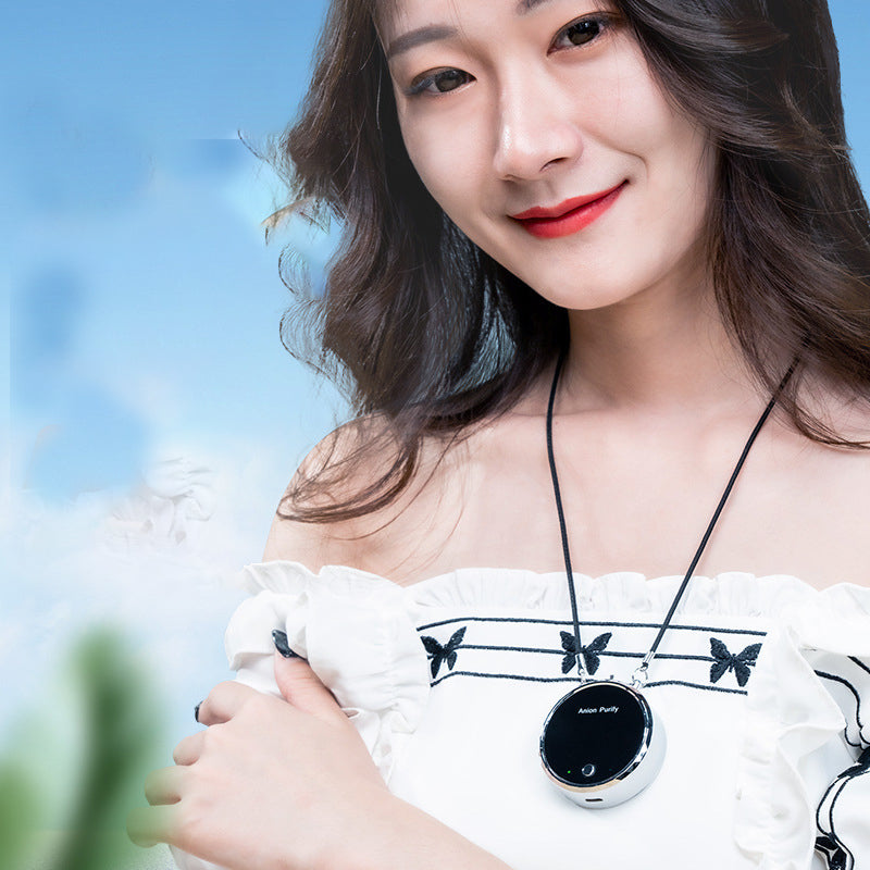 Woman wearing a white off-shoulder top with butterfly designs, holding a black and silver pendant.