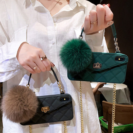 Two handbags with fur pom-poms, one black and one green, held by a person wearing a white shirt.