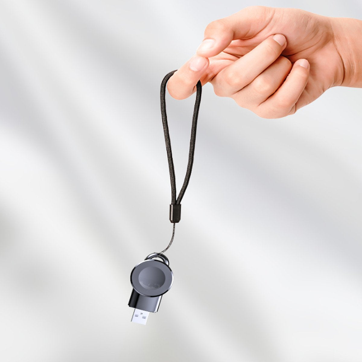 Hand holding a black lanyard with a small device attached against a light gray background
