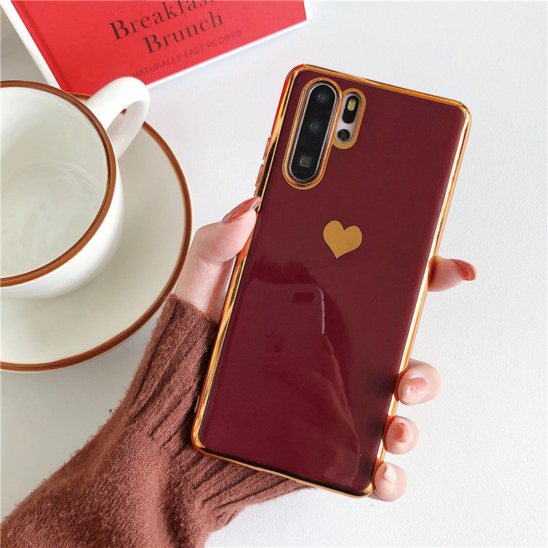 Phone case with a heart design held by a hand, next to a cup and saucer on a white surface.