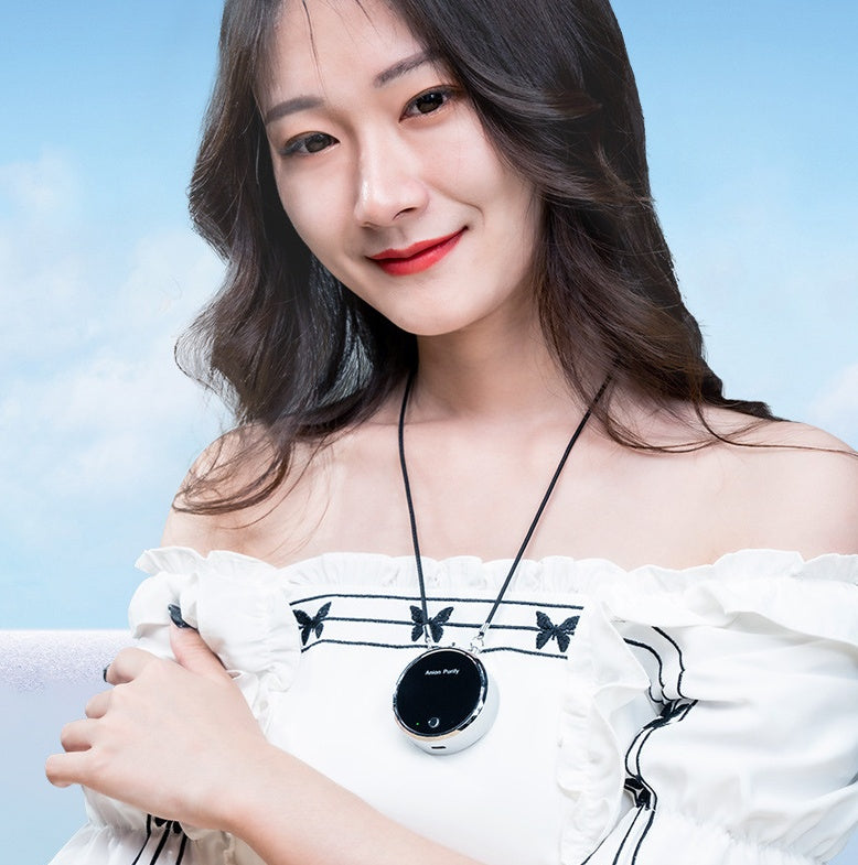 Woman wearing a white off-shoulder top with butterfly designs, holding a black and silver pendant against a light blue sky.
