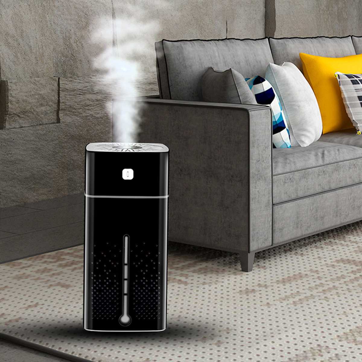 Black humidifier emitting steam in a living room with a gray sofa and colorful pillows.