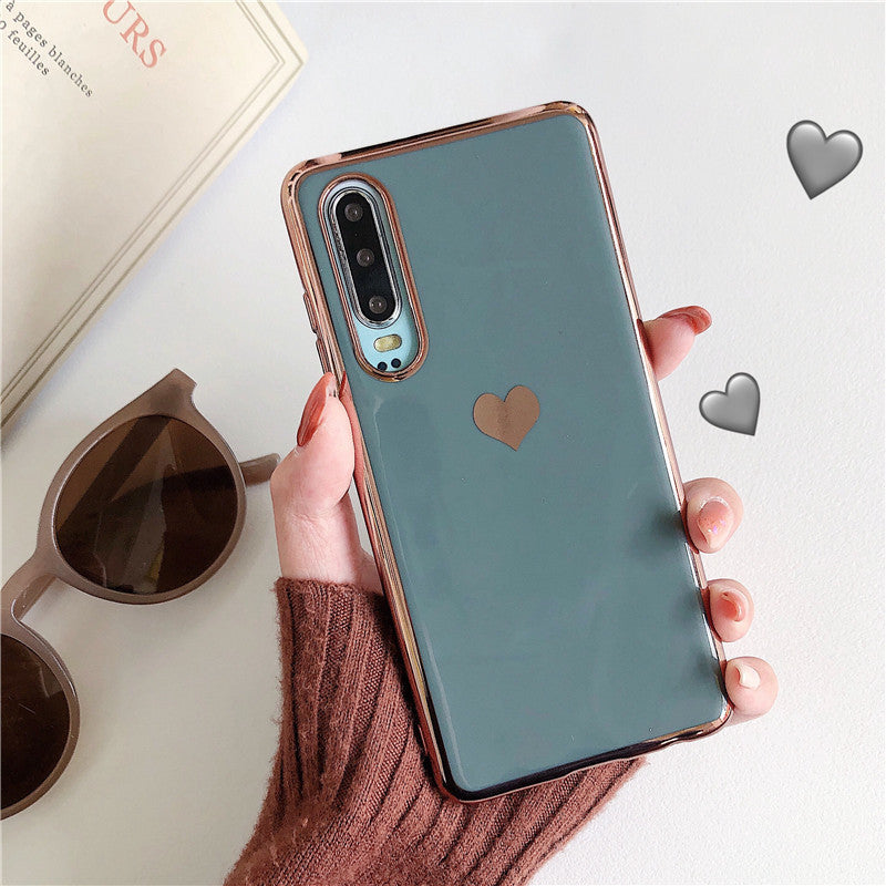 Phone case with heart design held by a hand, sunglasses and book in the background