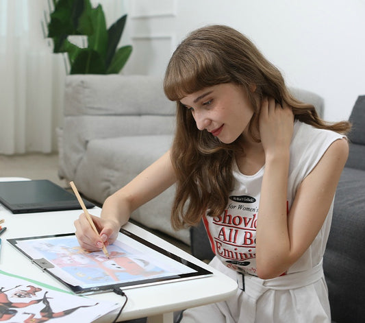 Woman sitting at a table with a tablet, drawing or painting, in a home setting.