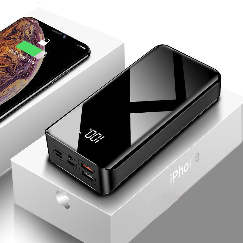 Black power bank with digital display on a white surface, next to a smartphone.