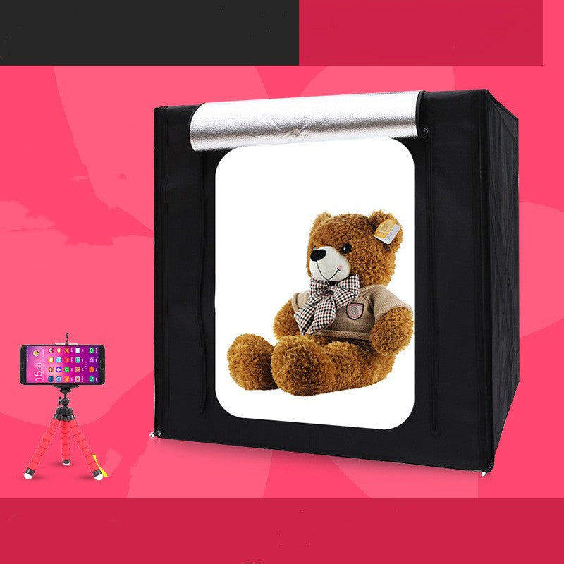 Teddy bear inside a photo studio box with a smartphone on a tripod outside the box.