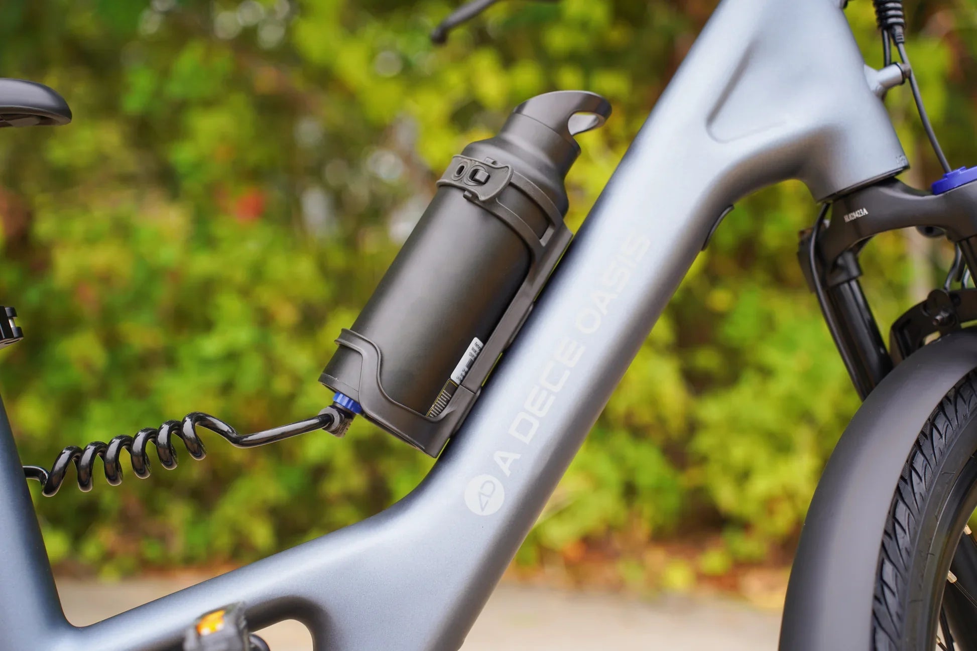 Bicycle water bottle holder attached to a bike frame with a blurred green background. best lightweight folding e-bike for city commuting. Raee -Industries