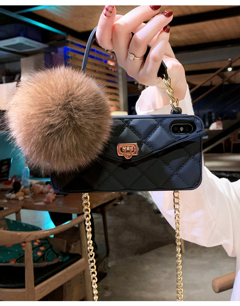 Black quilted phone case with gold chain and fluffy pom-pom held by a hand.